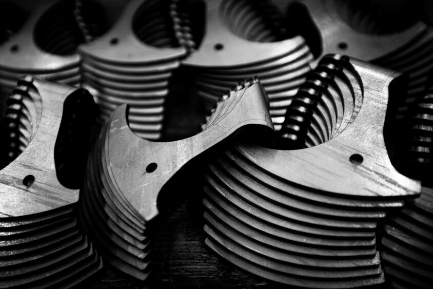 The black-and-white image captures a close-up of stacked metal components featuring fine milling structures and drill holes. The high-precision edges and symmetrical shapes reflect the exact manufacturing standards in prototyping at weba Germany. This image highlights the quality and precision essential for complex components in the automotive industry.