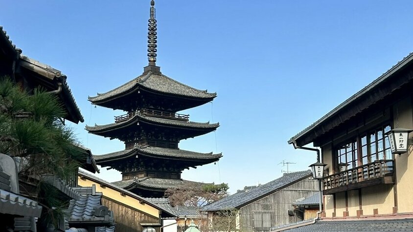 Eine traditionelle japanische Straße mit Holzhäusern und einer beeindruckenden Pagode im Hintergrund unter blauem Himmel.