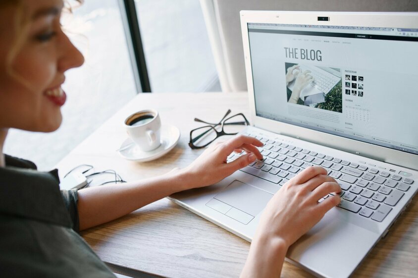 Photo of a woman working intently on a laptop. The laptop screen clearly shows “The Blog”, indicating that she is either writing a blog post or browsing blog content.