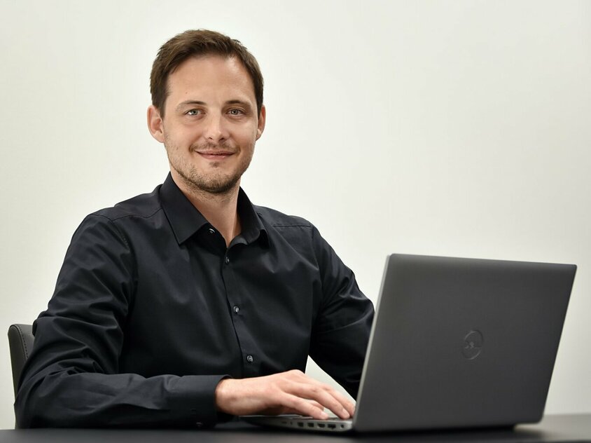 Ondrej Zima, Human Resource Manager der weba Olomouc sitzt avor einem geöffneten Laptop und  lächelt in die Kamera