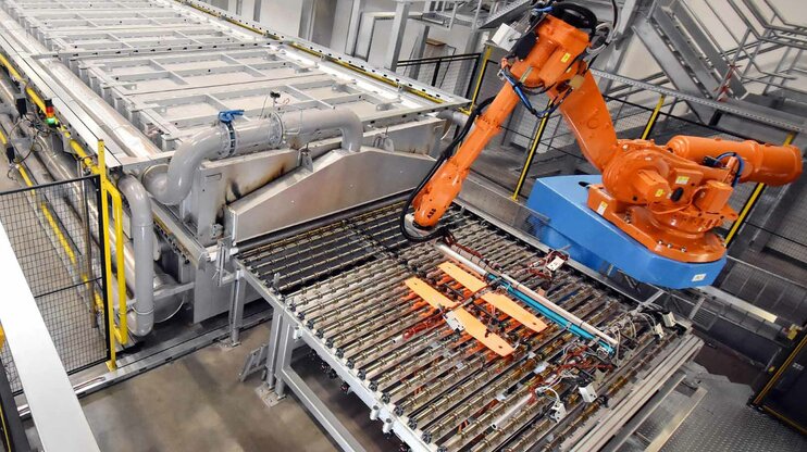 Roboterarm in einer automatisierten Produktionsanlage bei der Warmumformung, der glühend heiße Metallteile von einem Ofen zur Presse transferiert.