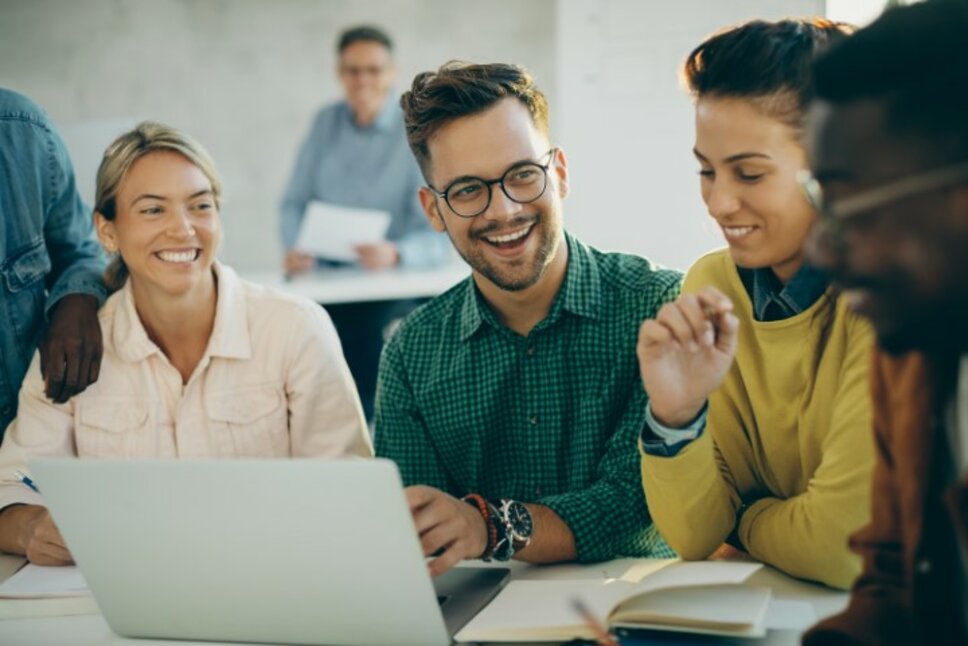 Fröhlicher Student hat Spaß beim Benutzen eines Laptops mit seinen Freunden im Klassenzimmer.